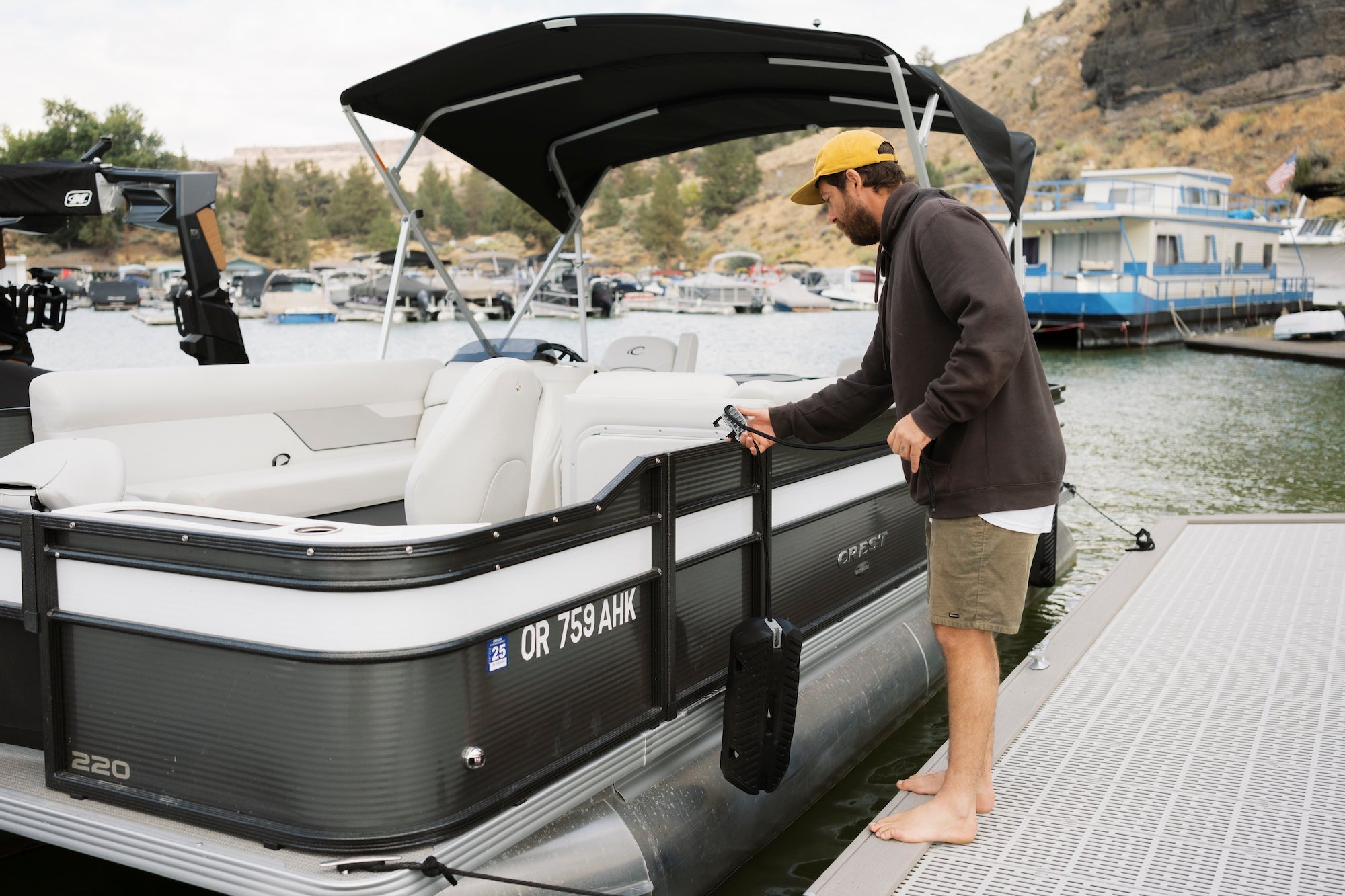 Man in a yellow hat securing a black Seipel Marine bumper to a pontoon boat at a dock.