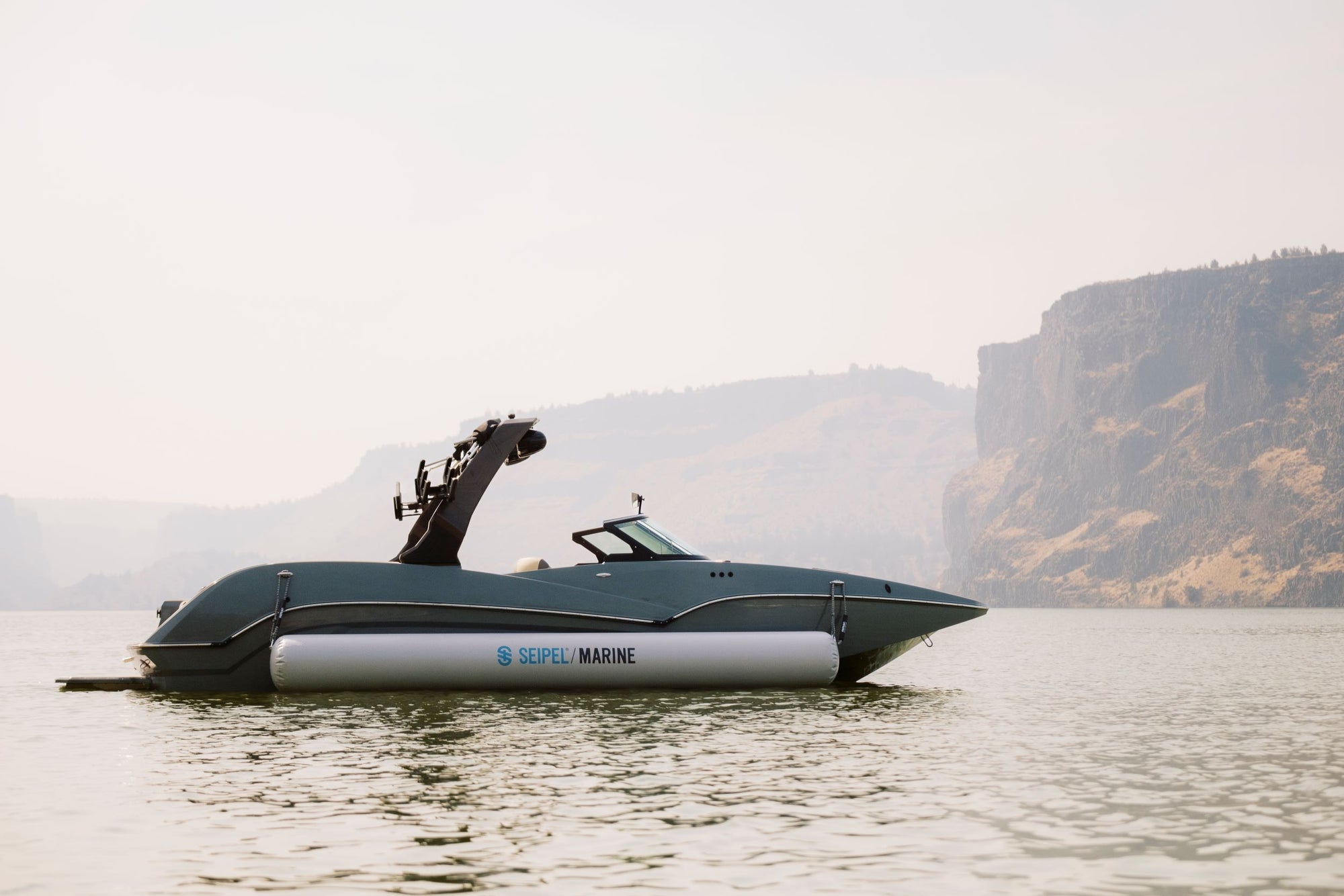 A sleek black boat with Seipel Marine inflatable side bumpers floating on calm water, with rocky cliffs in the background.