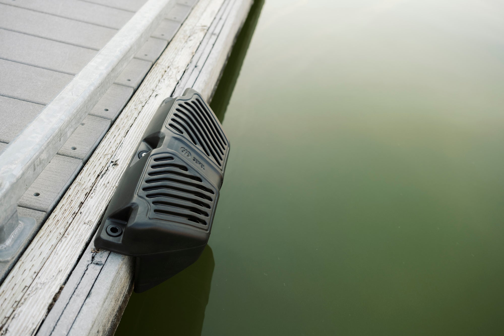 Black Seipel Marine Permanent Dock Fender secured on a gray deck with Green Lake Water Below..