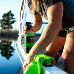 A woman cleaning a boat's surface with a green microfiber cloth while holding a bottle of Seipel Marine Water Spot Remover.