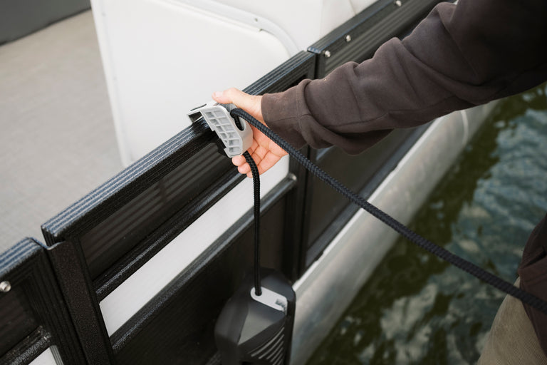 A person adjusting a gray pontoon fender hanger while securing a black rope to a boat railing.