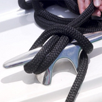 Close-up of a black braided dock line tied securely to a polished metal cleat on a white boat surface, with a hand adjusting the rope.
