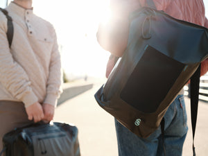 Lifestyle image of person wearing Backpack outdoors with front bottle pocket visible in sunlight.