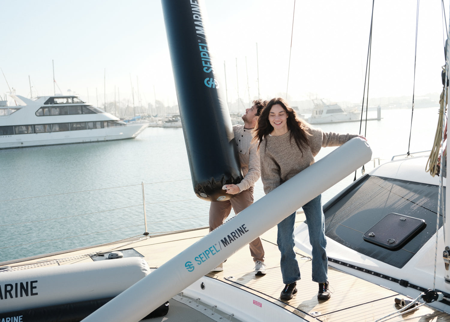 Two people carrying Seipel Marine inflatable dock bumpers across a boat deck.