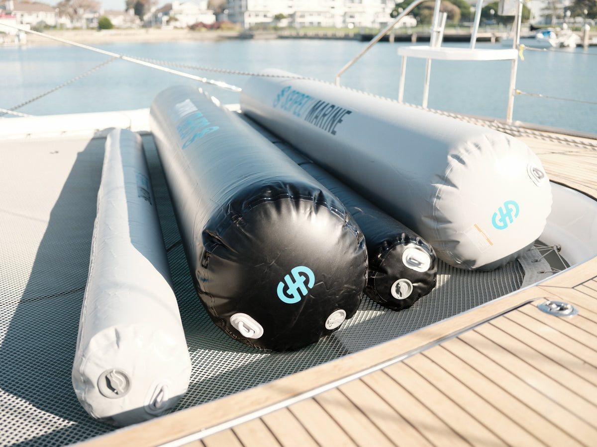 Four inflatable dock fenders in black and gray resting on a boat deck in sunlight.