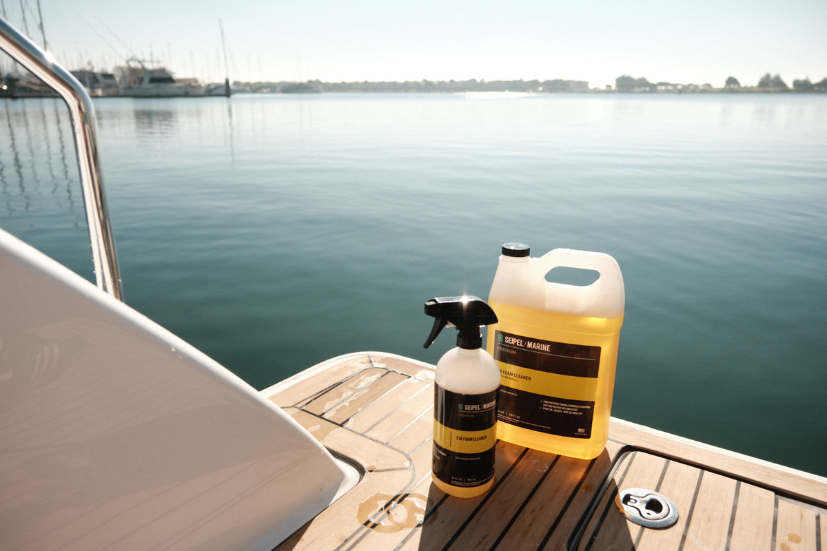 Seipel Marine EVA foam cleaner spray bottle and refill jug on a teak swim platform overlooking a marina.