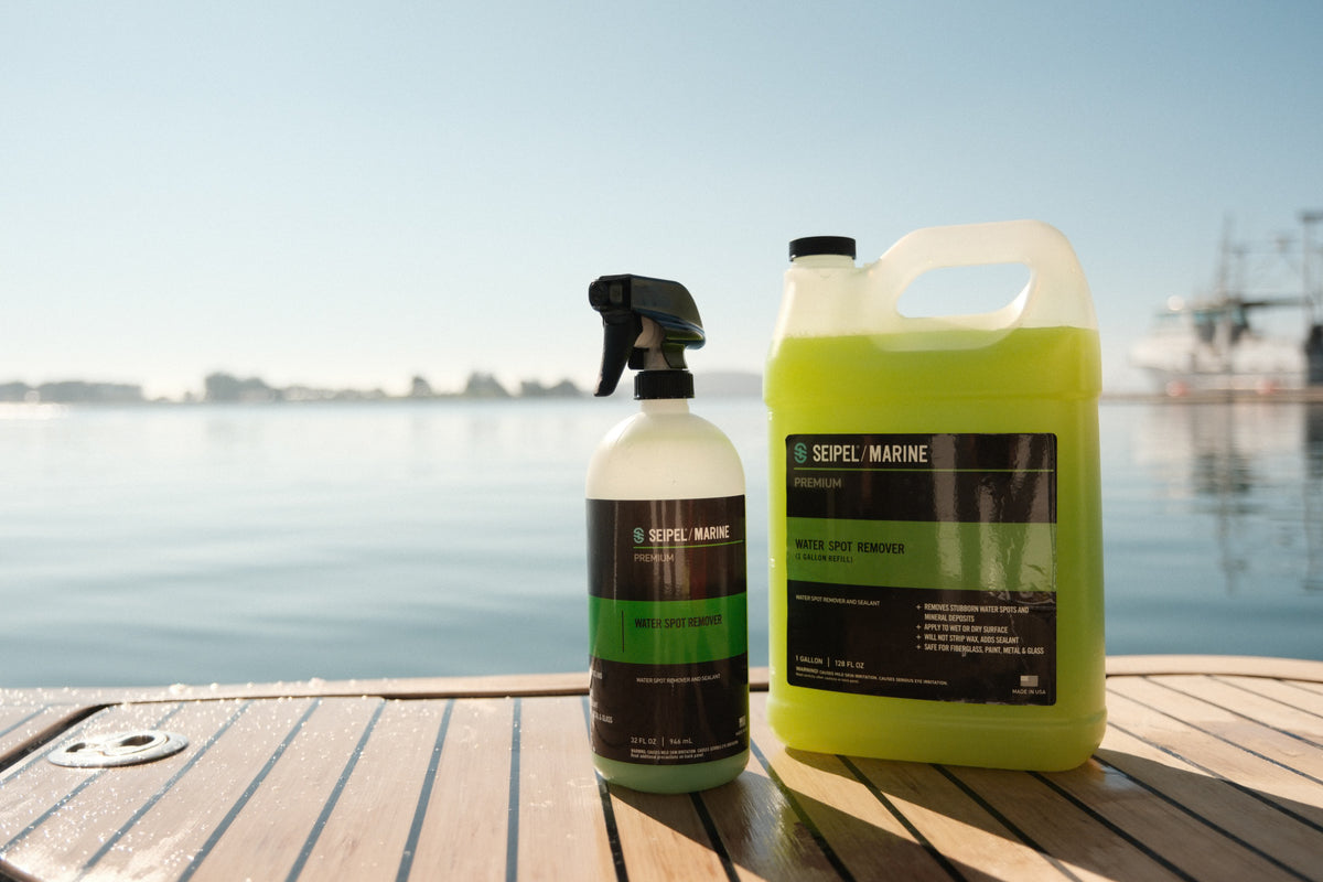 Close-up of Seipel Marine water spot remover spray bottle and refill jug on a boat deck by open water.