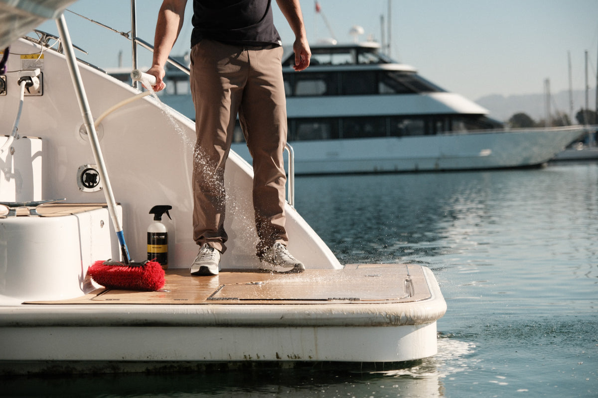 Person rinsing a boat swim platform with a hose, cleaning supplies visible on the deck.