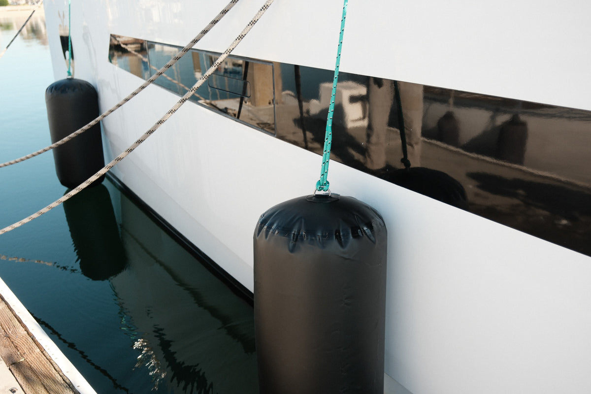 Boat tied at a dock with black cylindrical fenders hanging along the hull.