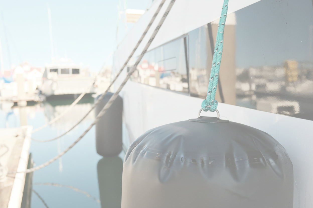 Close-up of gray inflatable boat fender hanging from a rope alongside a docked vessel.