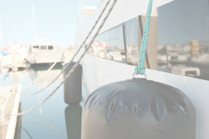 Close-up of gray inflatable boat fender hanging from a rope alongside a docked vessel.