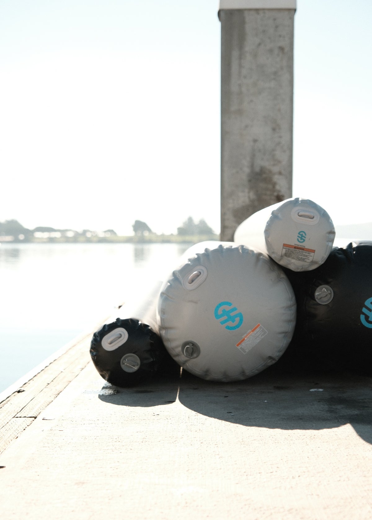 Stacked black and gray inflatable fenders resting on a dock near calm water.