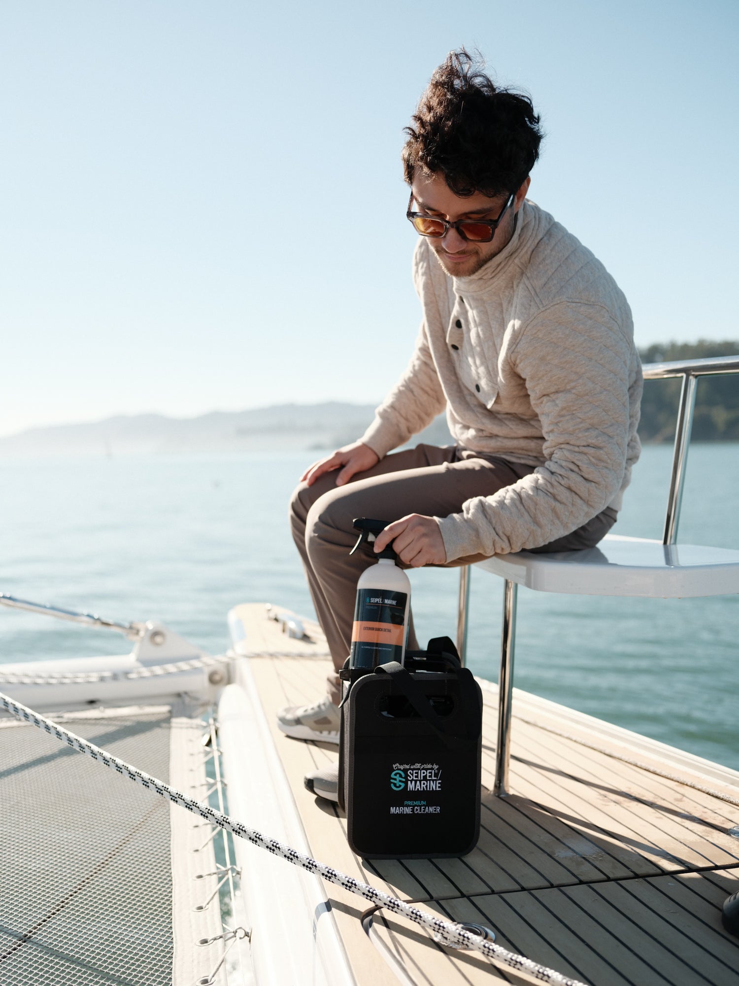 Person seated on a boat holding a spray bottle next to a Seipel Marine cleaning kit.