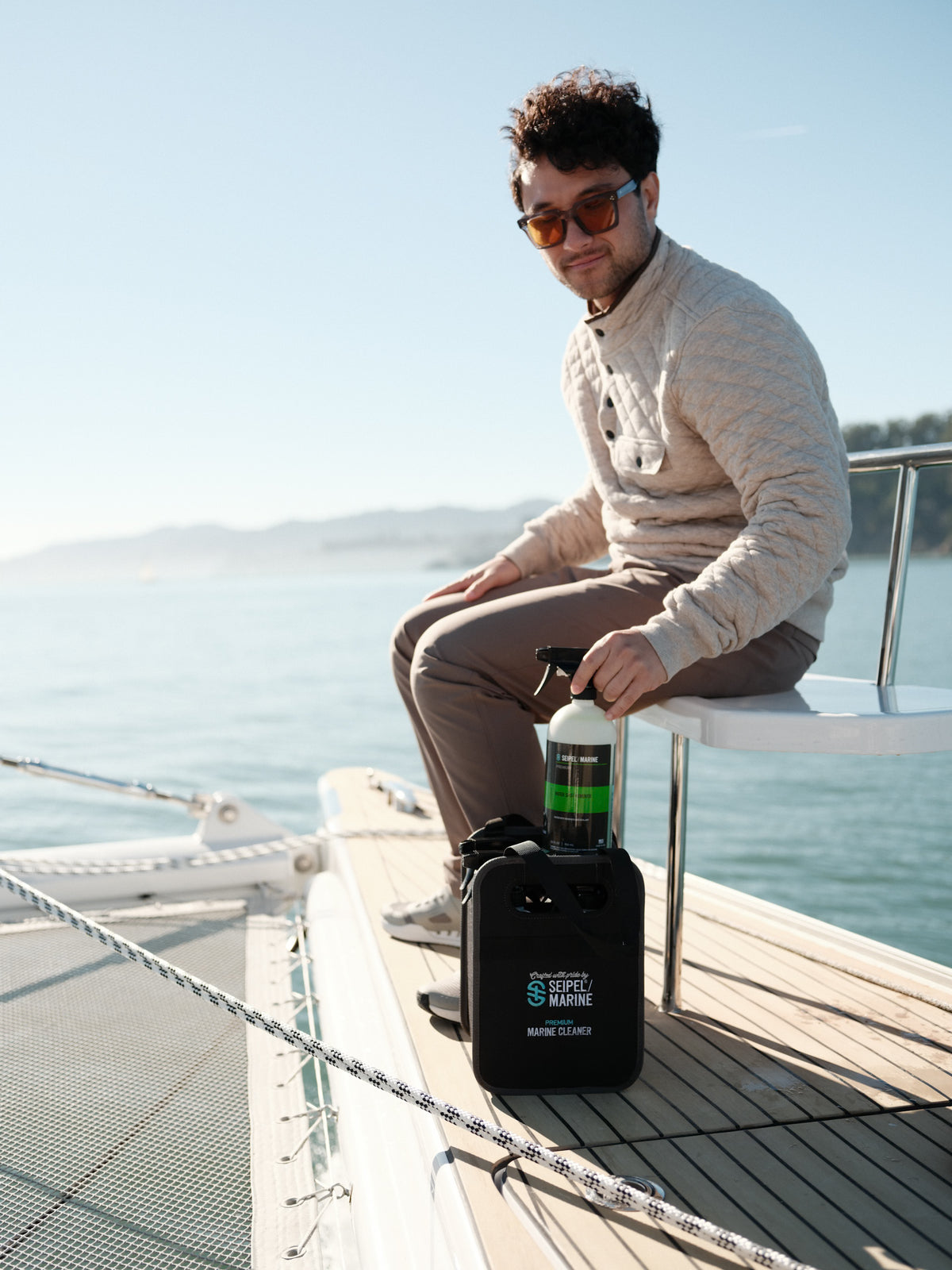 Person seated on a boat holding a spray bottle next to a Seipel Marine cleaning kit.