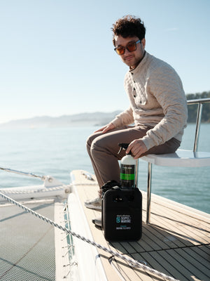 Person seated on a boat holding a spray bottle next to a Seipel Marine cleaning kit.