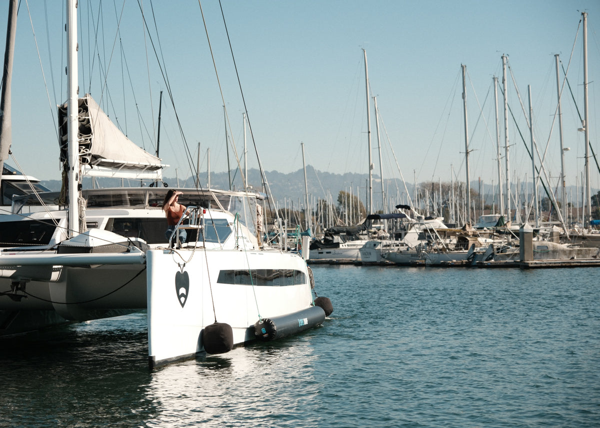 Catamaran docked at a marina with black fenders hanging along the hull.
