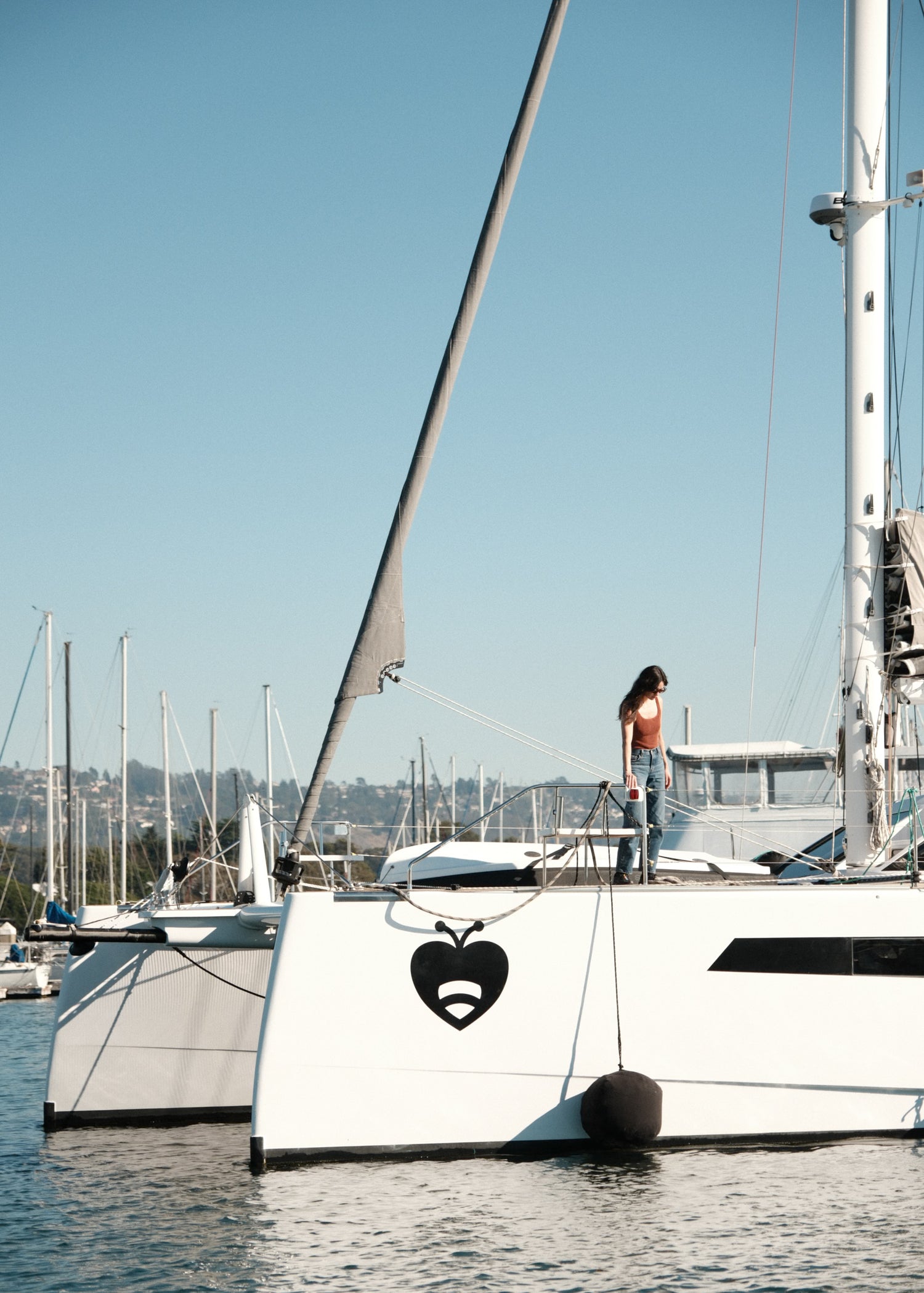 Person standing on a catamaran deck with a black inflatable fender tied to the hull.