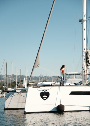 Person standing on a catamaran deck with a black inflatable fender tied to the hull.