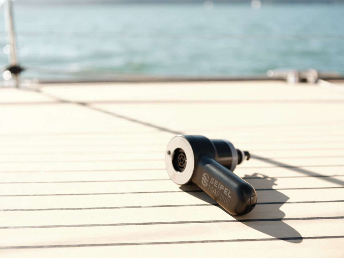 Handheld electric inflator resting on a boat deck with water in the background.