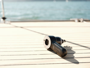 Handheld electric inflator resting on a boat deck with water in the background.