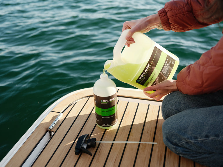 Person pouring Seipel Marine water spot remover from a jug into a spray bottle on a boat deck.